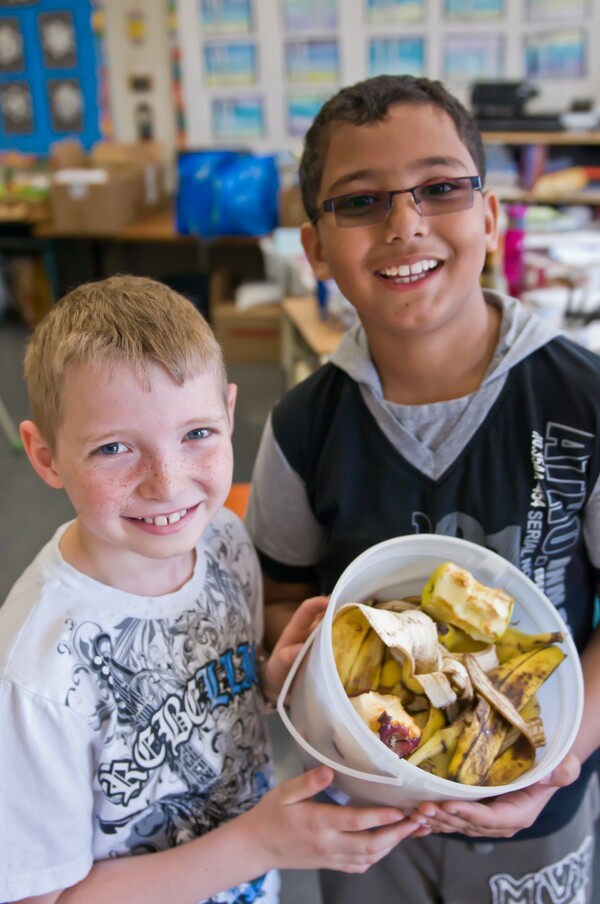 two boys holding a container of food scraps