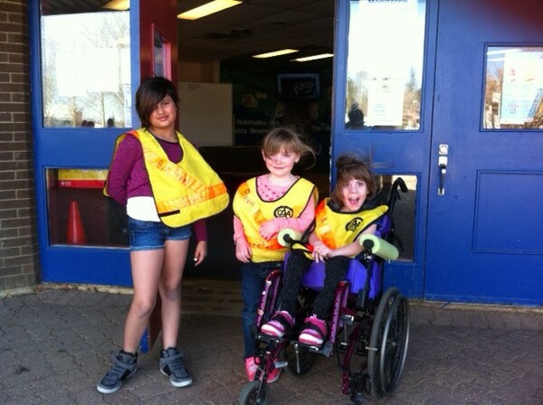3 kids wearing yellow vests outside of school